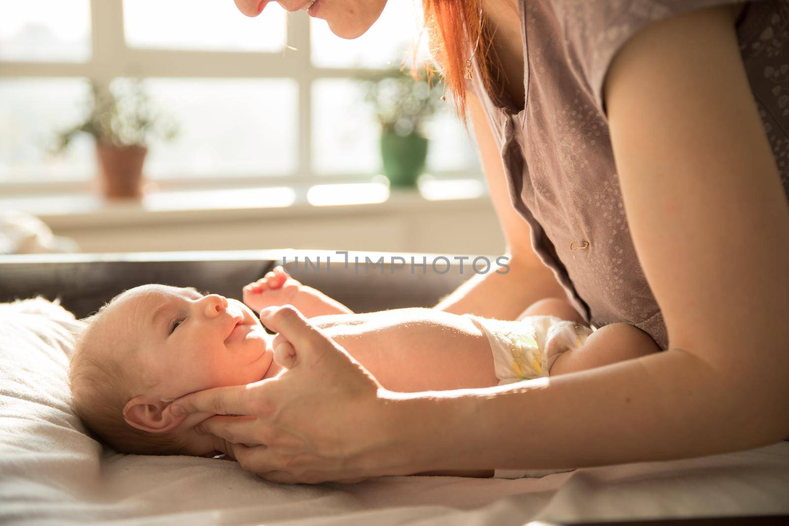 Mother takes care and holding her little baby lying on a bed by Studia72