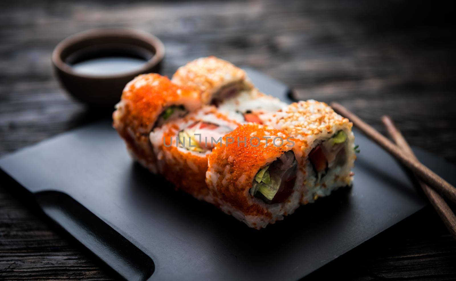 close up of sushi rolls on black tray and dark wooden table