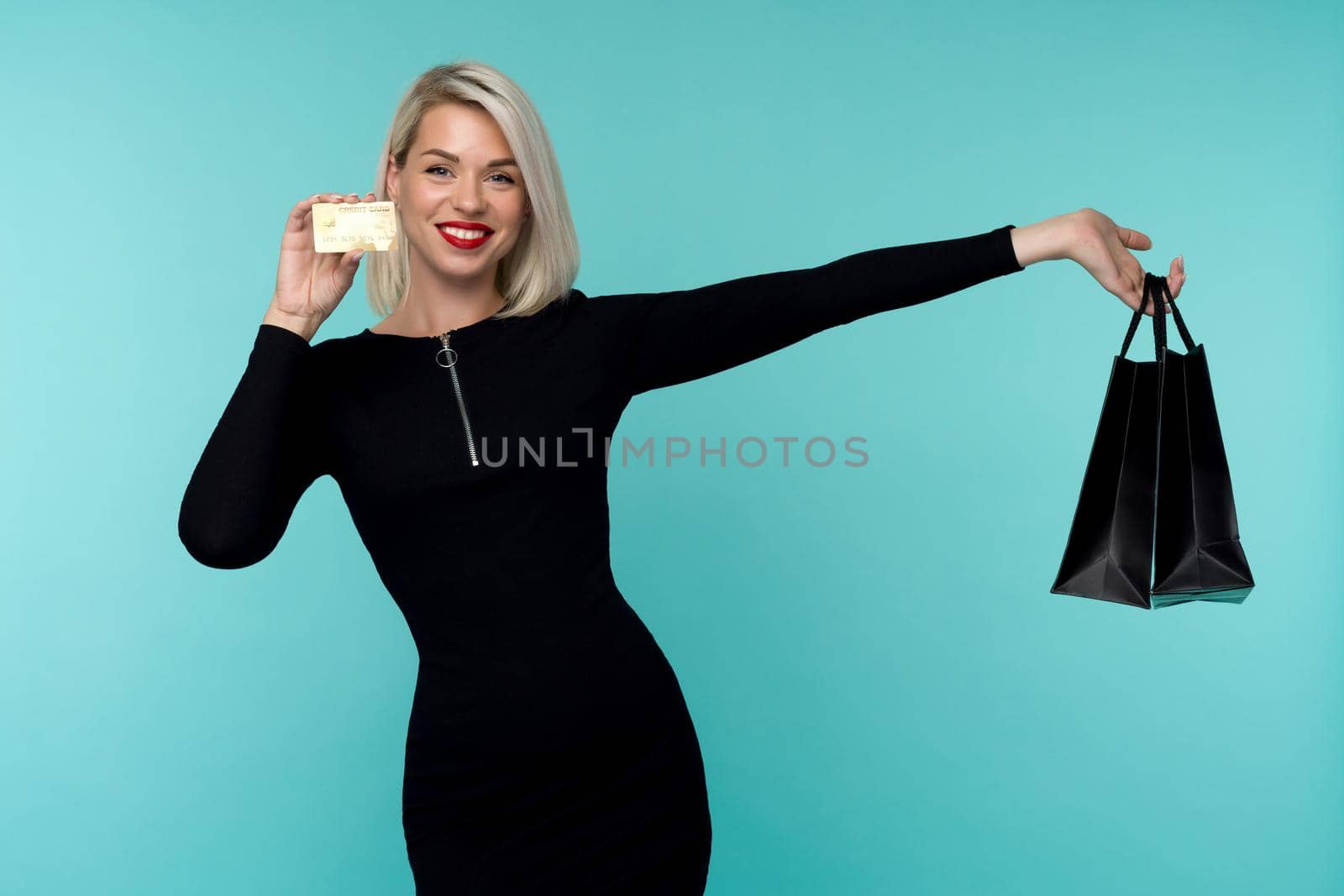 Image of a beautiful happy young blonde woman posing isolated over blue wall background holding shopping bags. Black Friday Holiday Concept. Sale