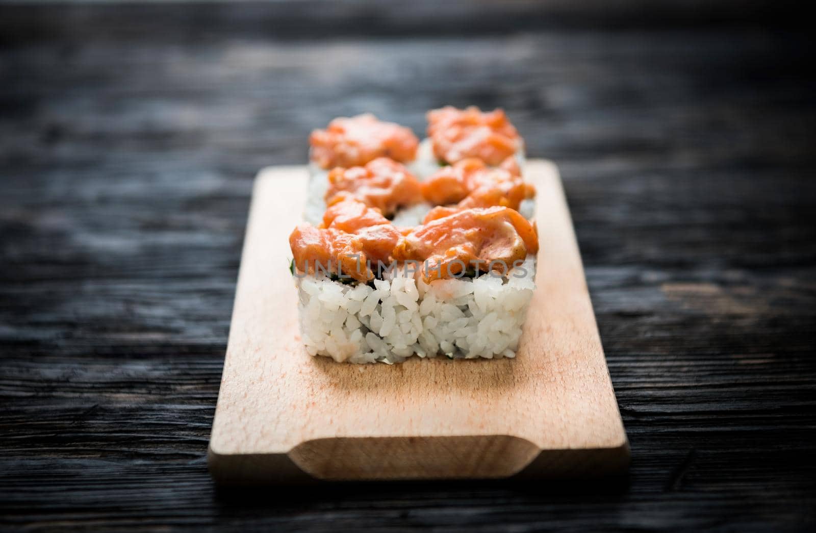 closeup of a set of sushi rolls with salmon topping on wooden board