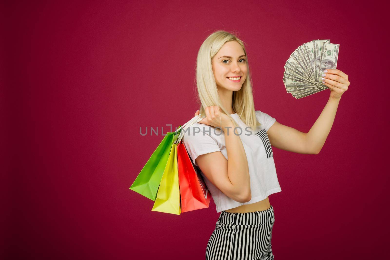 Happy girl in holds one hundred dollars bills and shopping bags on ruby background