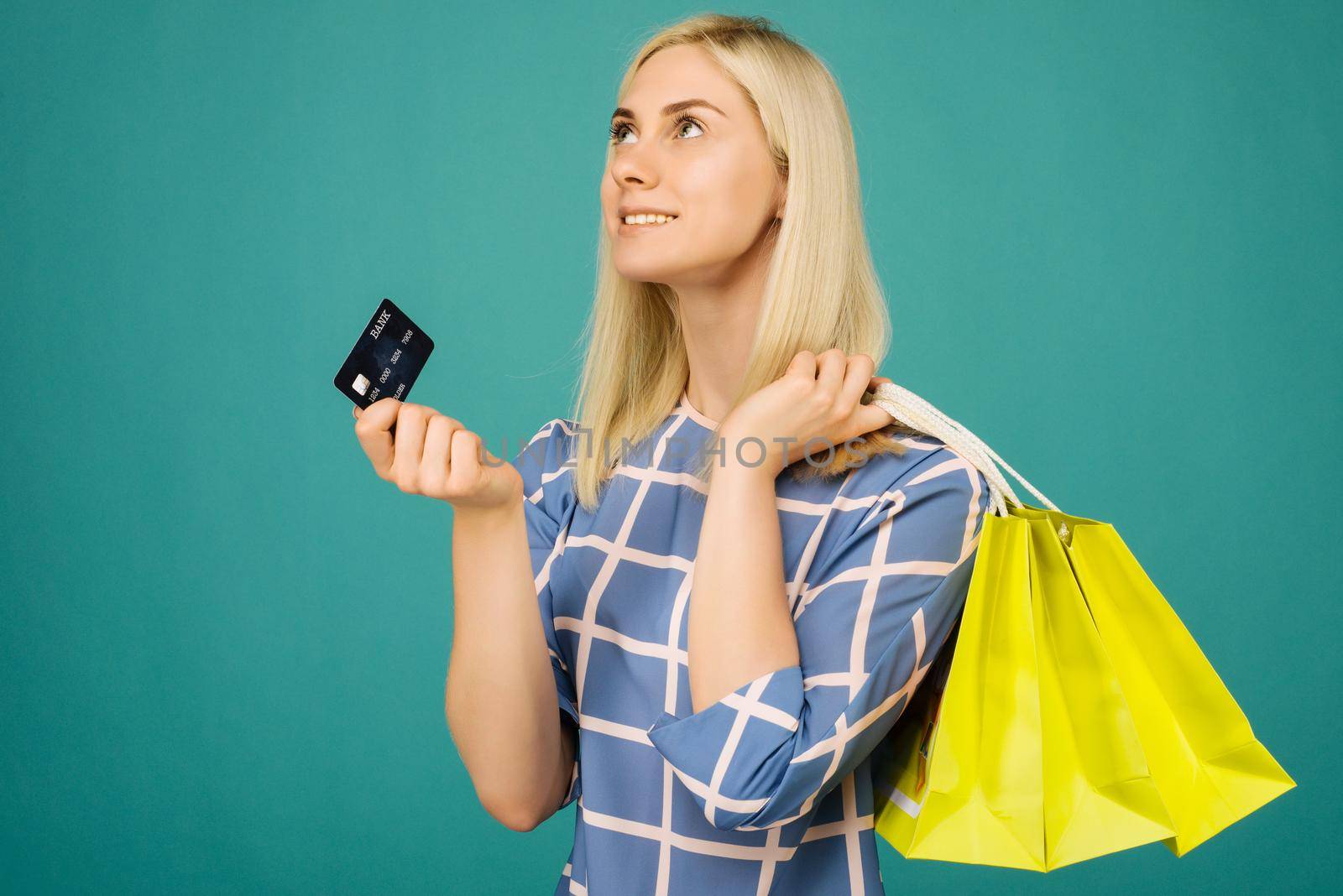 Happy girl in a checkered blouse holds credit card and shopping bags on blue background