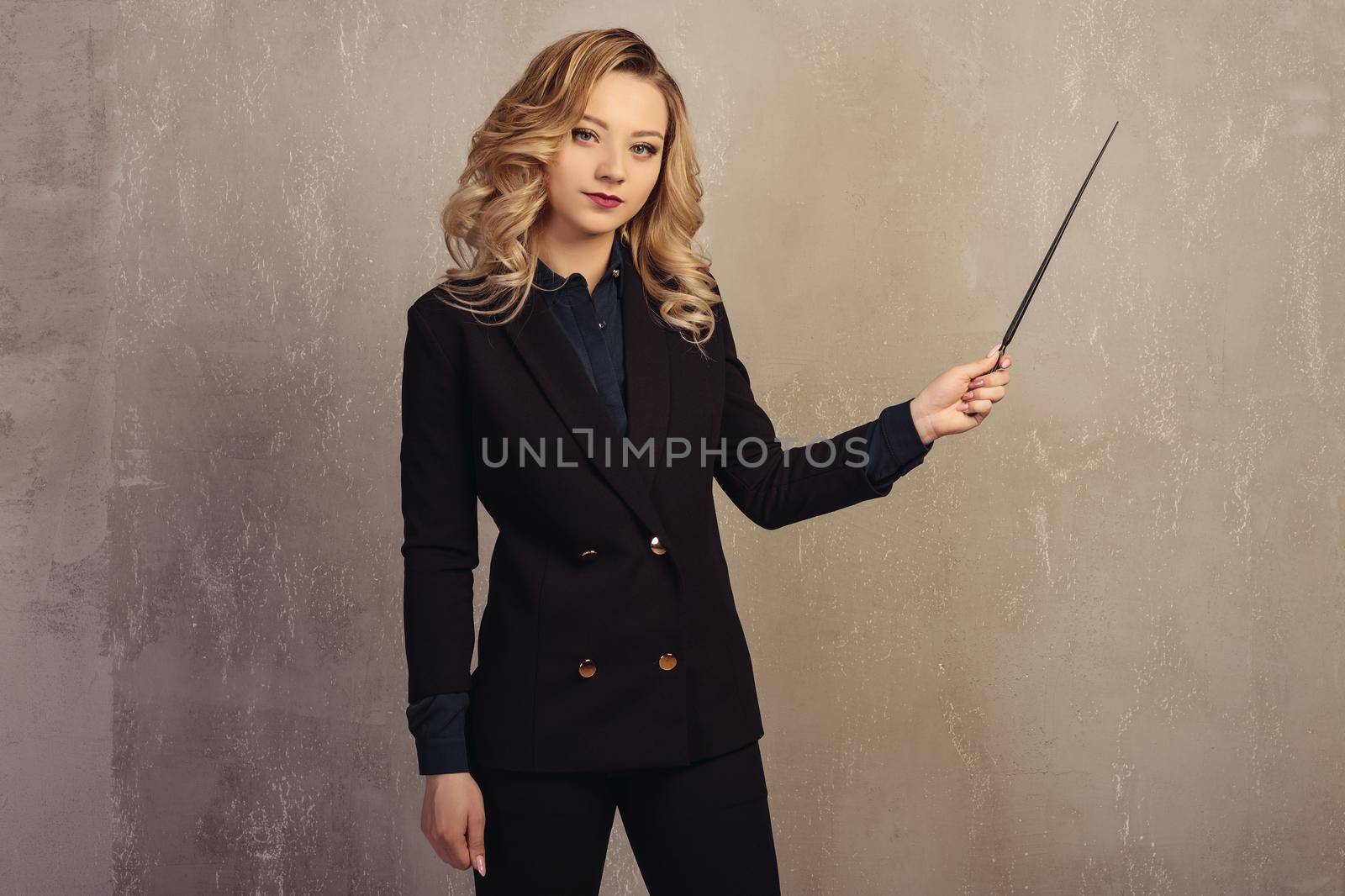 Young beautiful woman teacher with pointer in hand near a gray textured wall.
