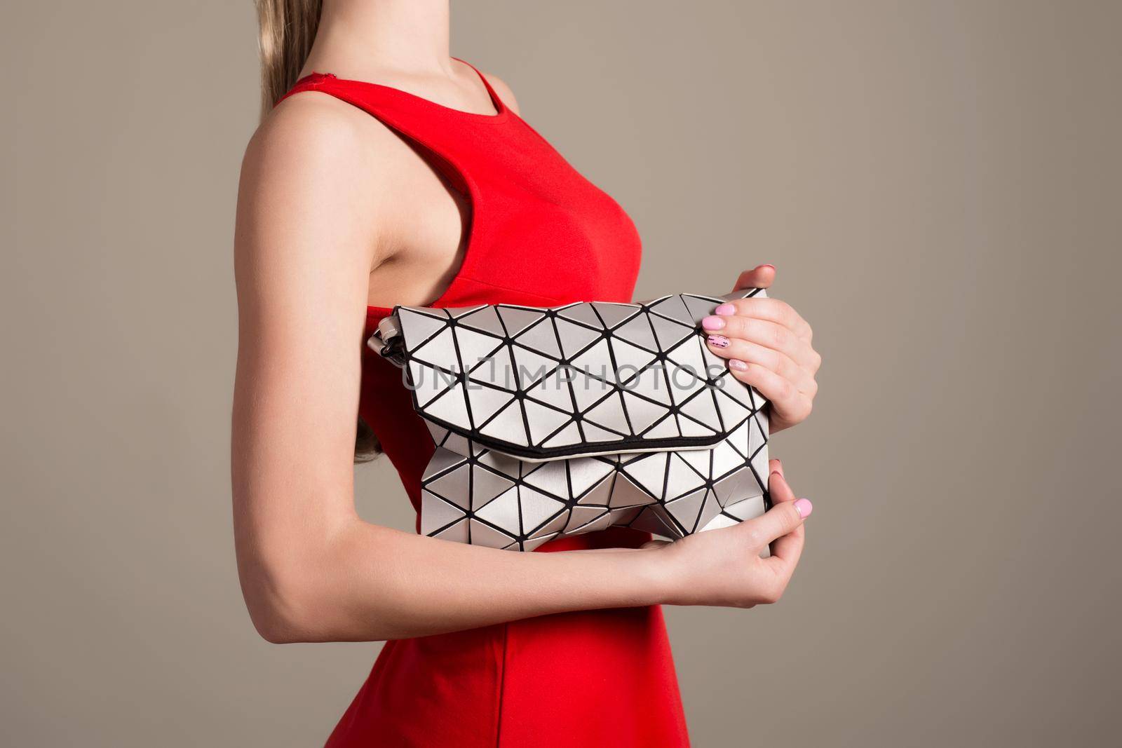 Attractive slim girl in a red evening dress holds a stylish bag of silvery triangles by zartarn