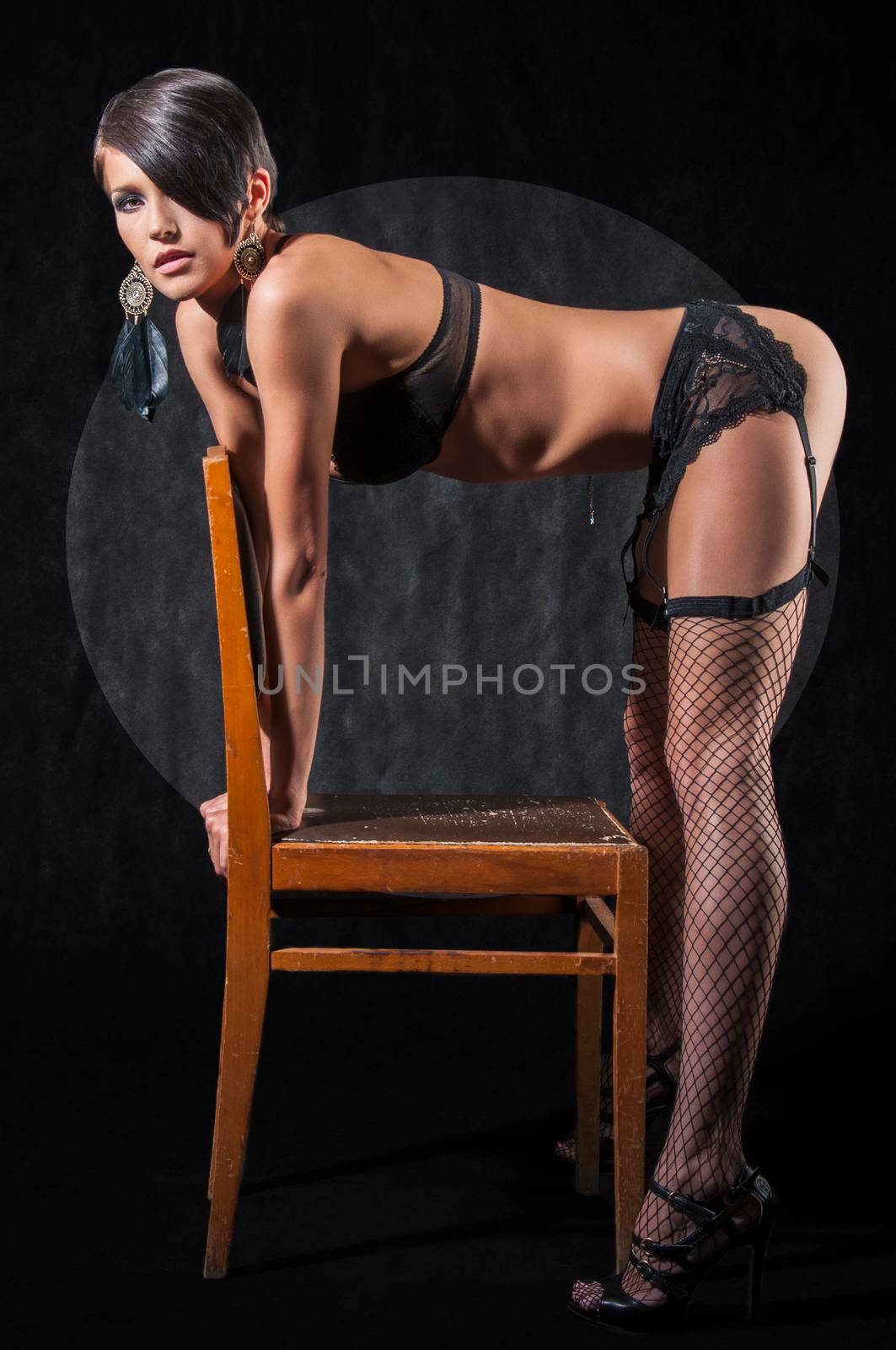 Sensual brunette woman bent over chair, posing in sexy underwear