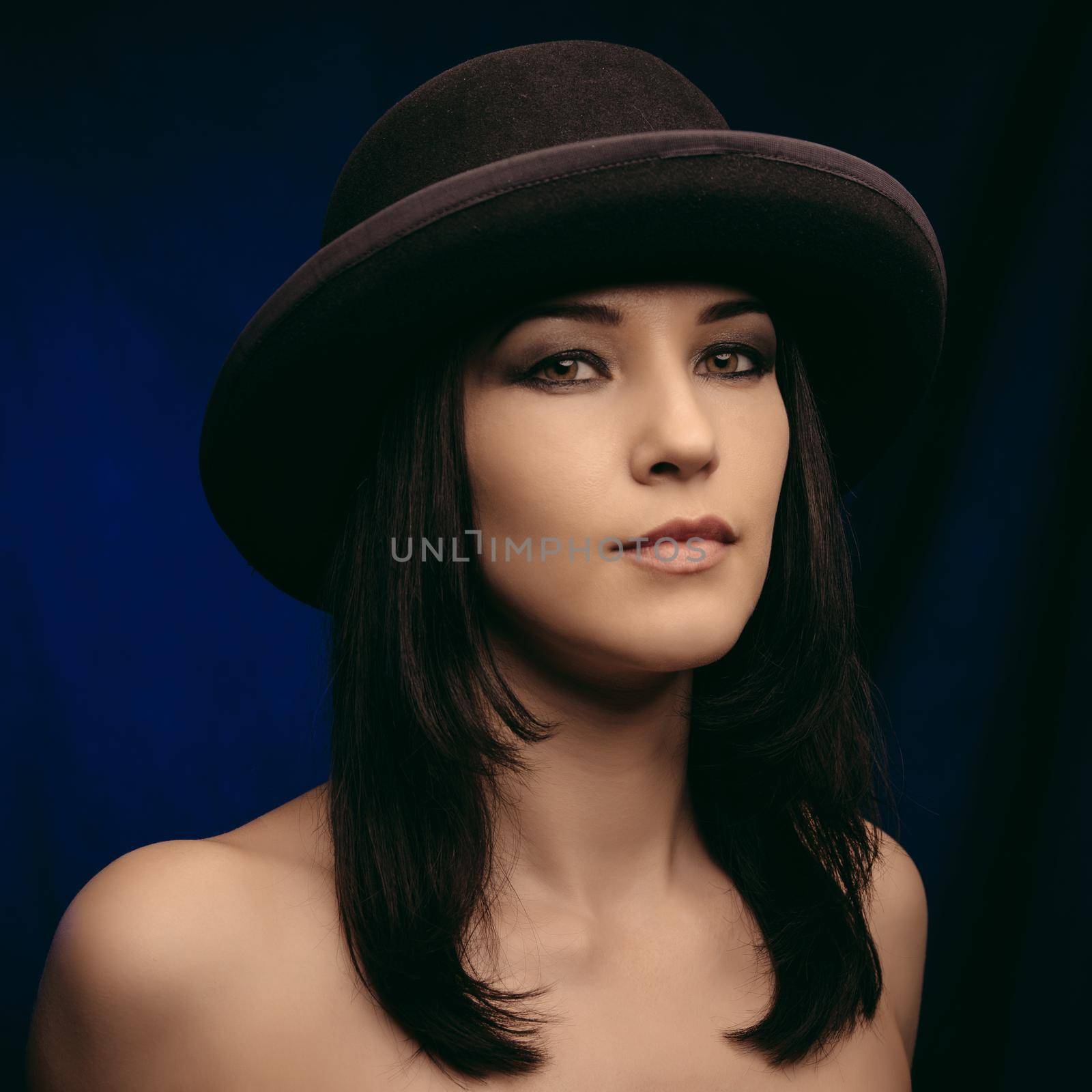 Happy smiling female model in black elegant hat on blue background.
