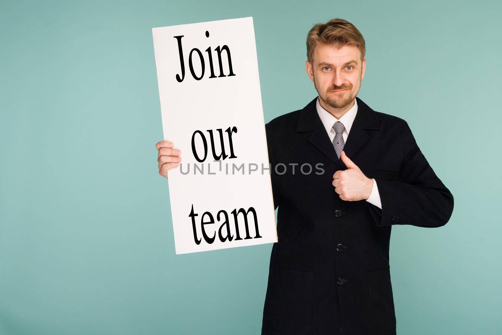 Happy smiling young business man showing signboard with sign Join Our Team thumbs up, on blue background