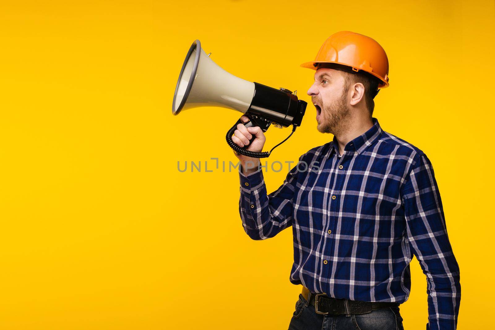 Angry worker man in orange helmet with a megaphone on yellow background - Image