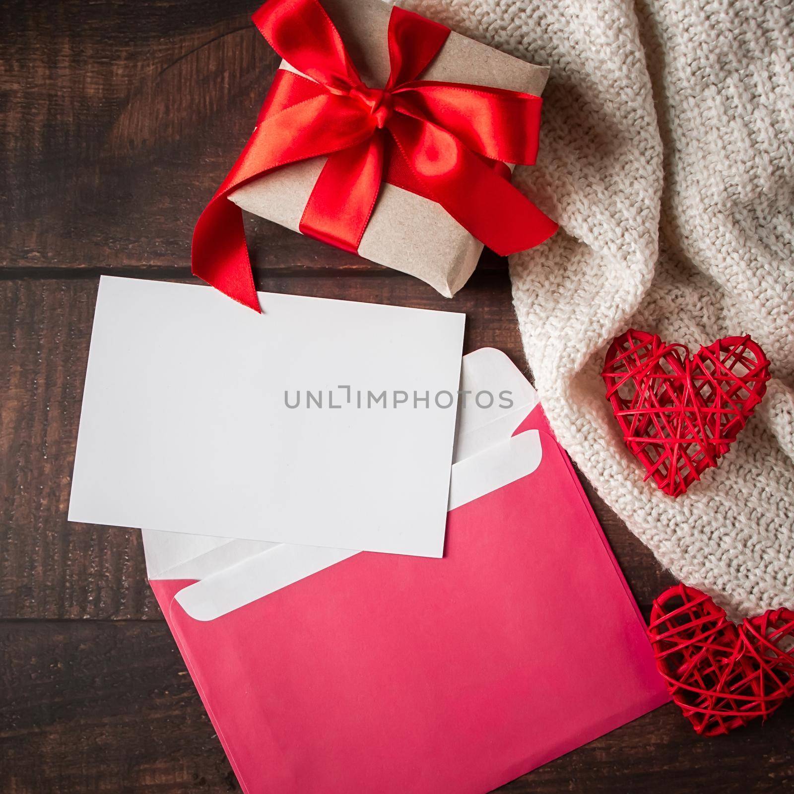 Envelope and greeting card on a wooden background. Gift with a red ribbon and an envelope with a card on a background of red hearts. Layout for Valentine's Day.