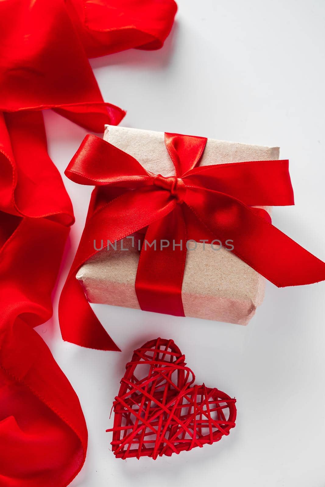 Gift box with craft paper and red ribbon on a white background. Valentine's day design concept - gift box and heart on a white background, vertical photo