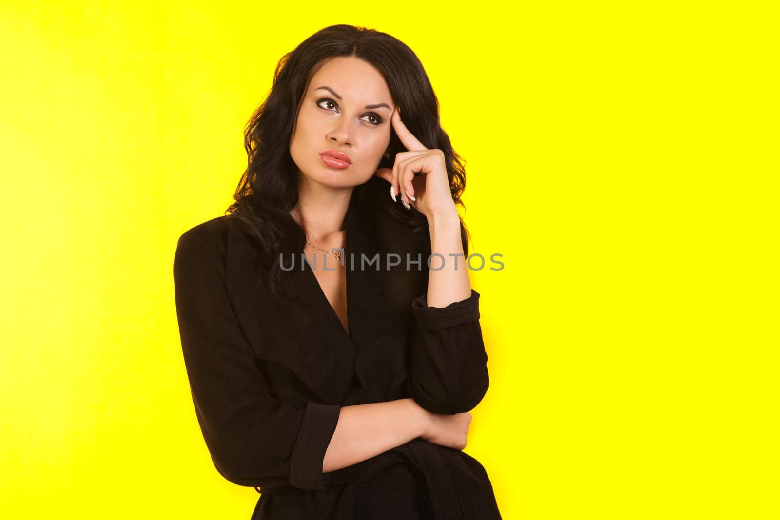 Pensive businesswoman holds finger near forehead. Isolated portrait on yellow background