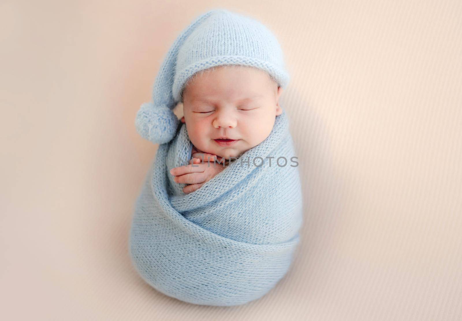 Newborn baby boy swaddled in blue fabric sleeping. Infant child kid resting during studio photoshoot