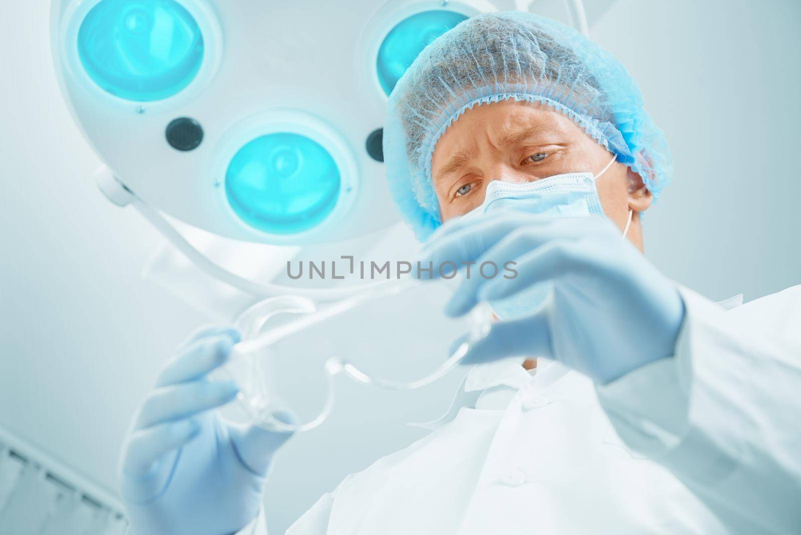 Young man surgeon takes off his protective glasses after operation in hospital