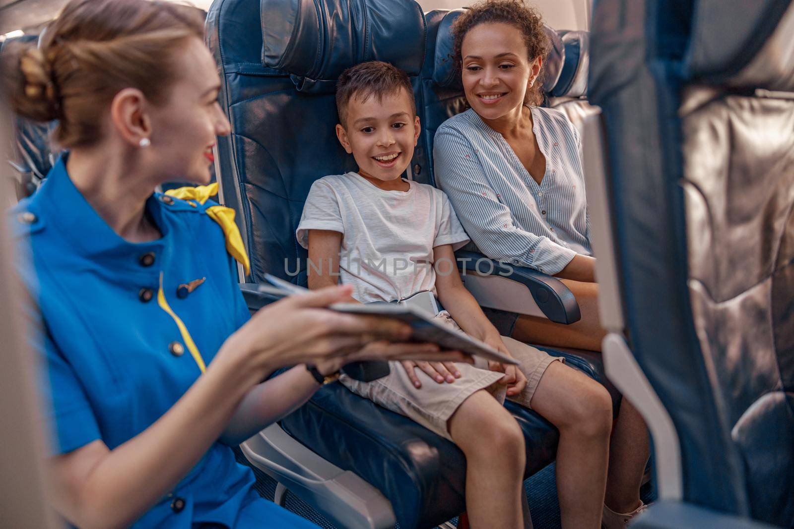 Female air hostess trying to entertain a kid on the plane by offering a book to read. Cabin crew provide service to family in airplane by Yaroslav_astakhov