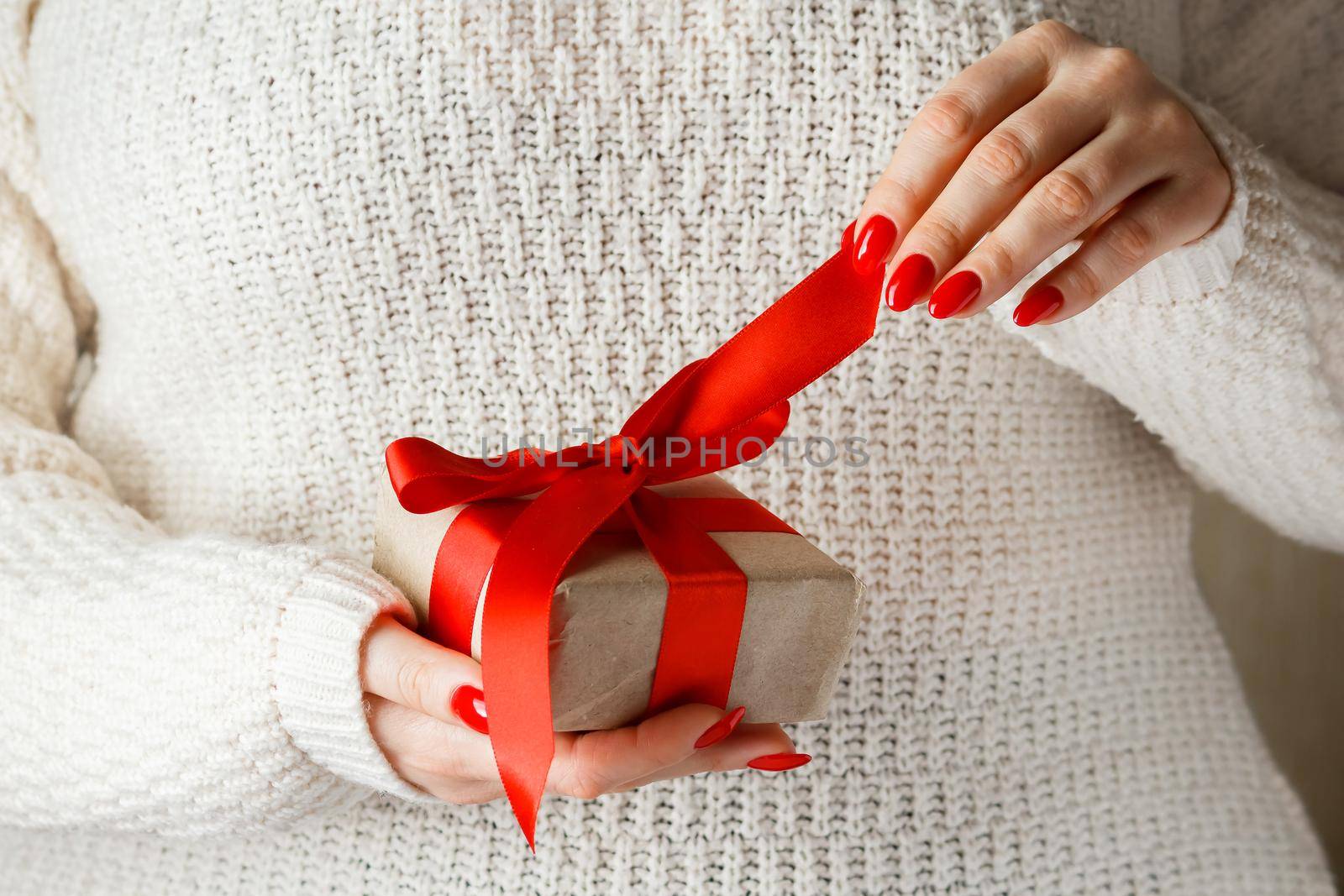 Gift with a red ribbon in hands on a white background. Woman unpacks a beautiful gift with a scarlet ribbon for mother's day.
