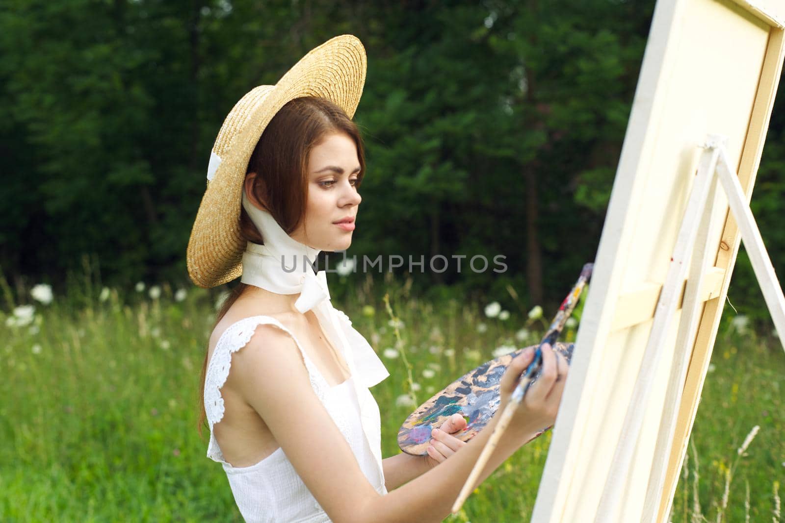 pretty woman in hat artist paints a picture on nature paint. High quality photo