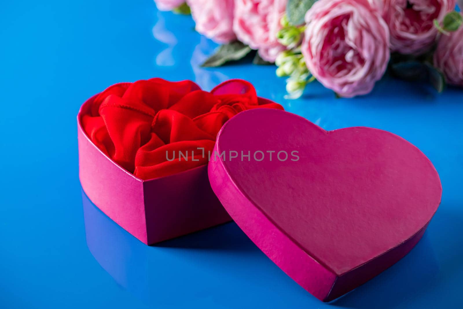 Heart shaped open gift box on blue background. Gift for Valentine's Day. Open pink box in the shape of a heart and flowers close-up.