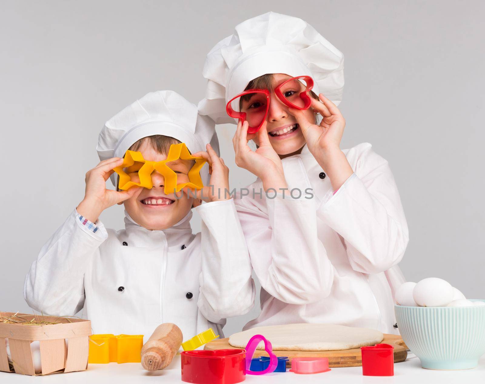 two funny children play in the kitchen with forms for dough cutting