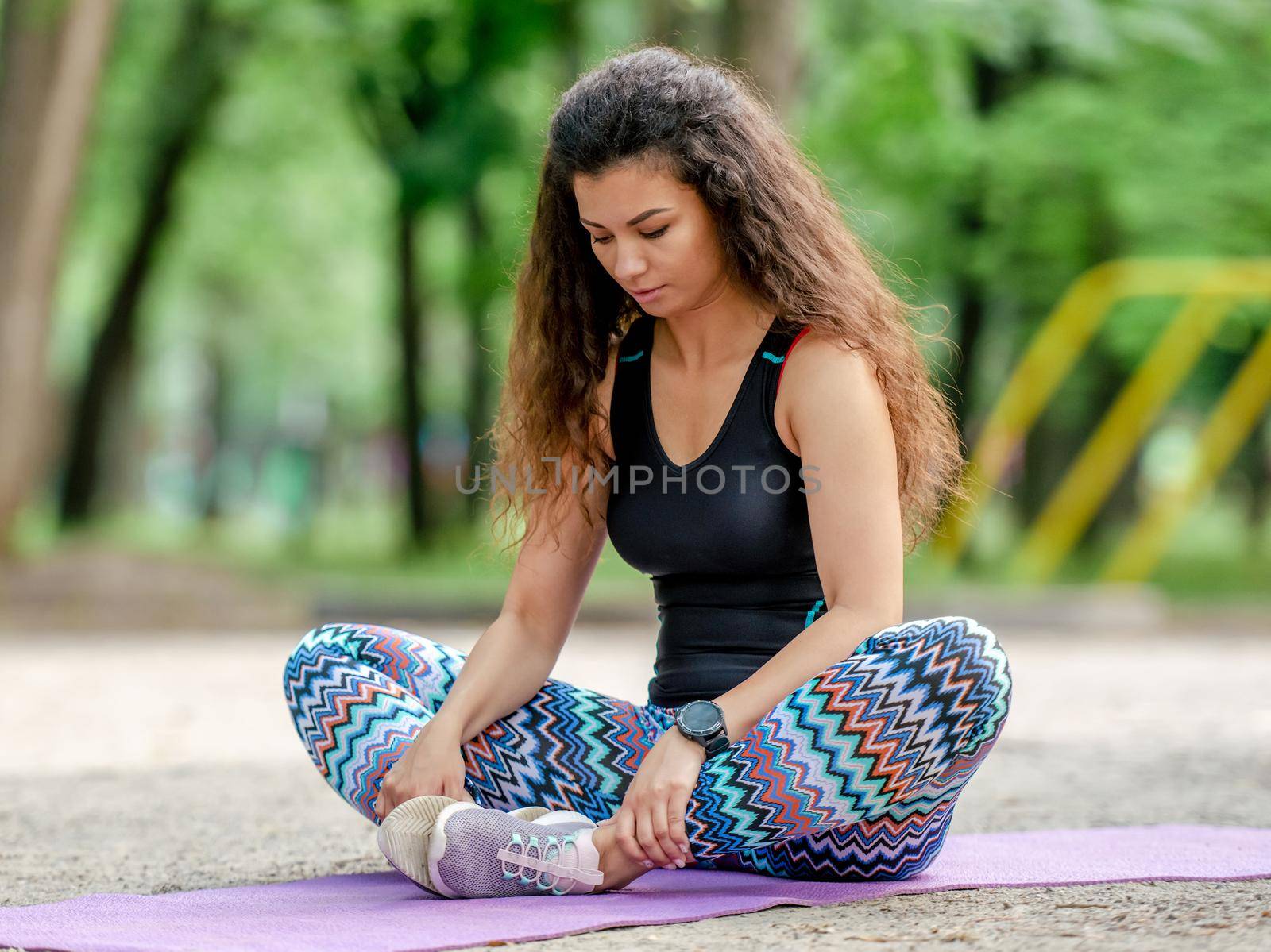 Girl stretching in butterfly pose outdoors at stadium. Pretty woman doing yoga workout at summertime