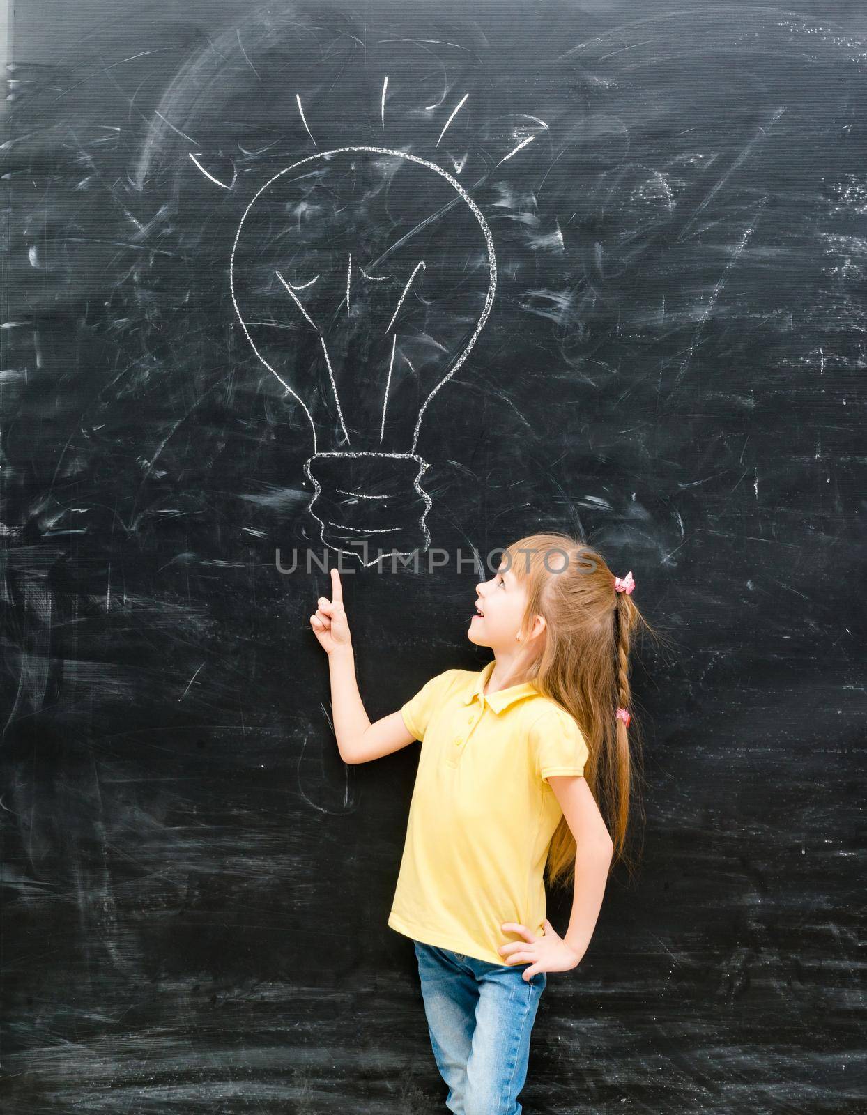 cute little girl pointing on a drawn lamp on chalky blackboard