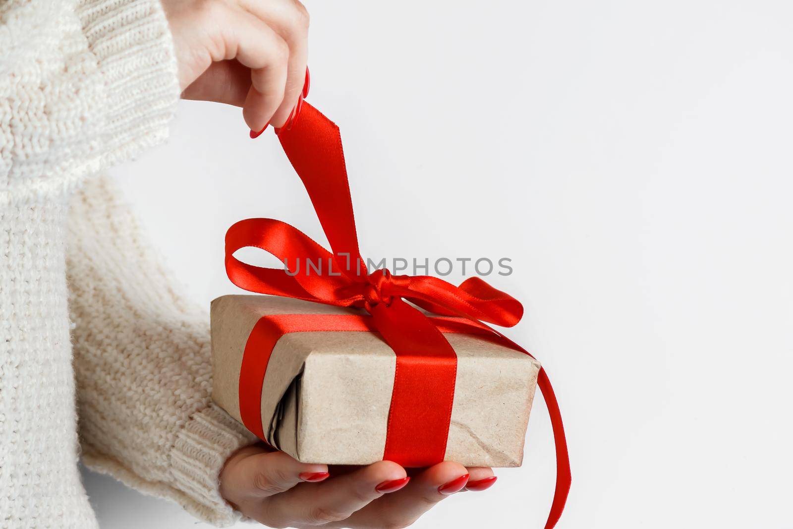 Gift with a red ribbon in hands on a white background. Woman unpacks a gift with a red ribbon on a white background.