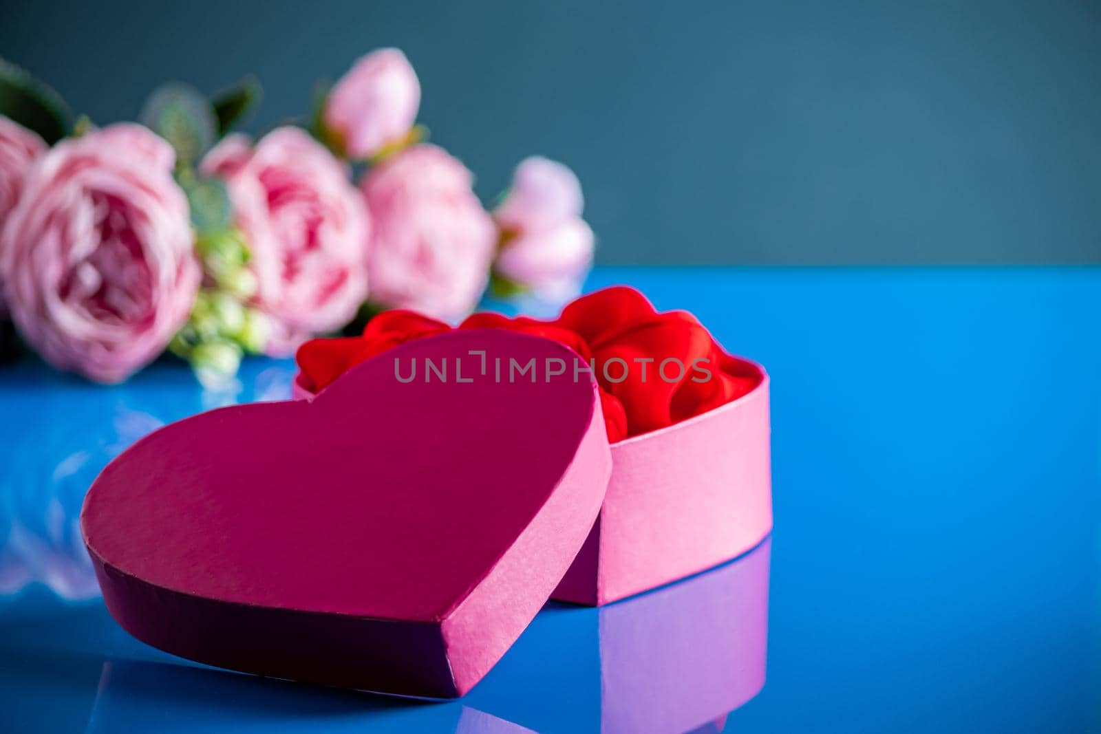 Heart shaped open gift box on blue background. by Statuska