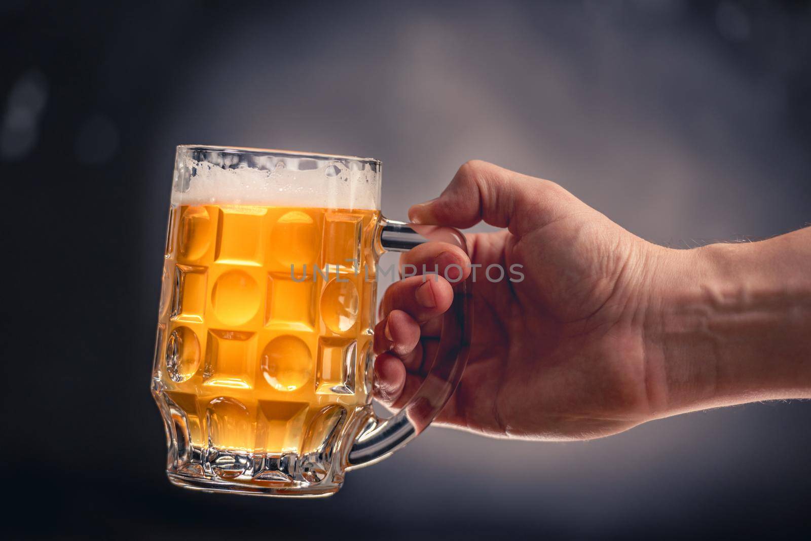 Hand holding full beer mug isolated on dark grey background