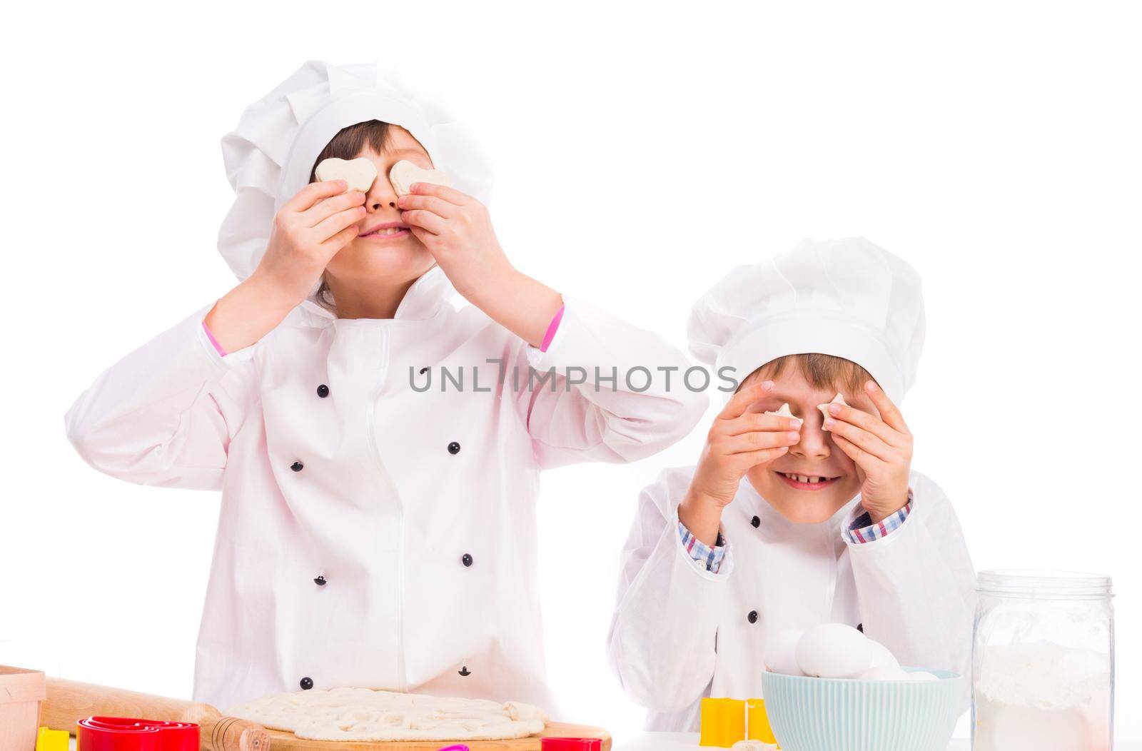 two little cooks in white uniform holding pieces of dough like eyes