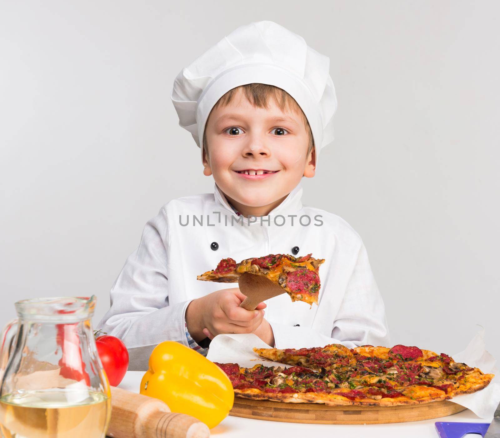 funny little boy in cook uniform holding a piece of tasty pizza