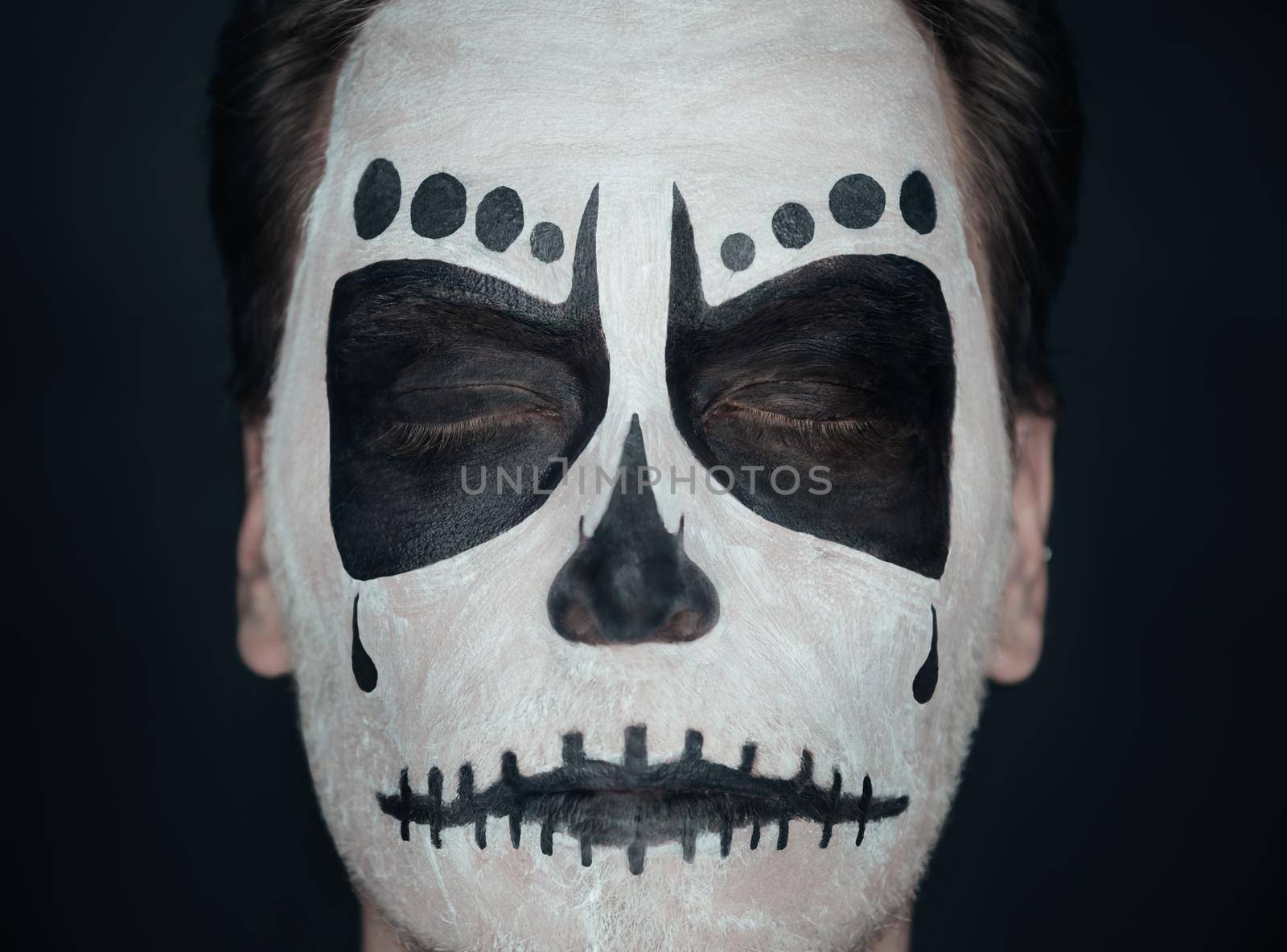 Portrait of young man with closed eyes and sugar skull makeup. Halloween face art