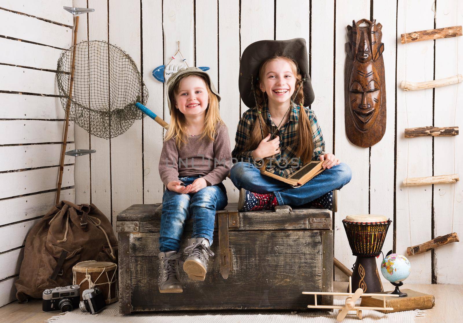 two cute little girls sitting on big wooden chest in cowboy hats