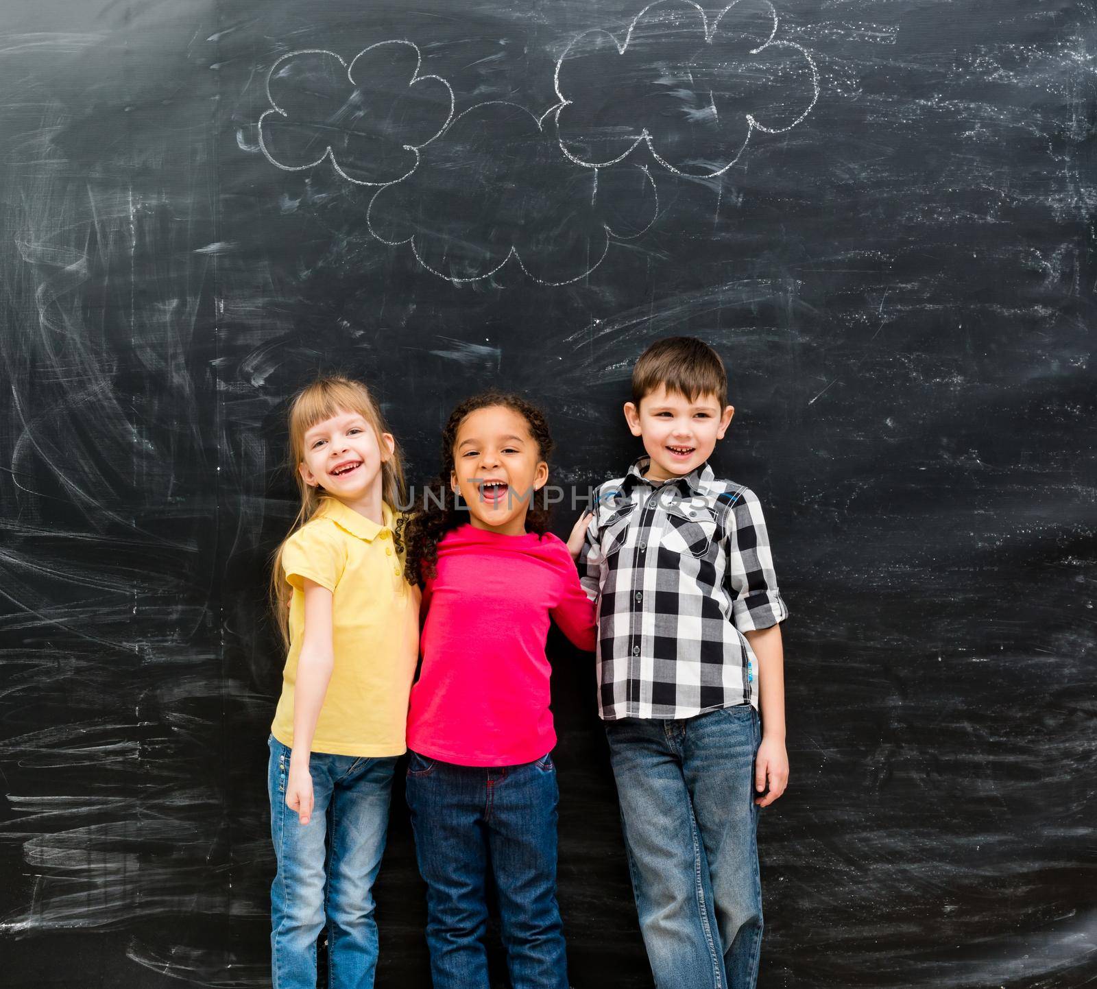 three different laughing children with blackboard on background having fun