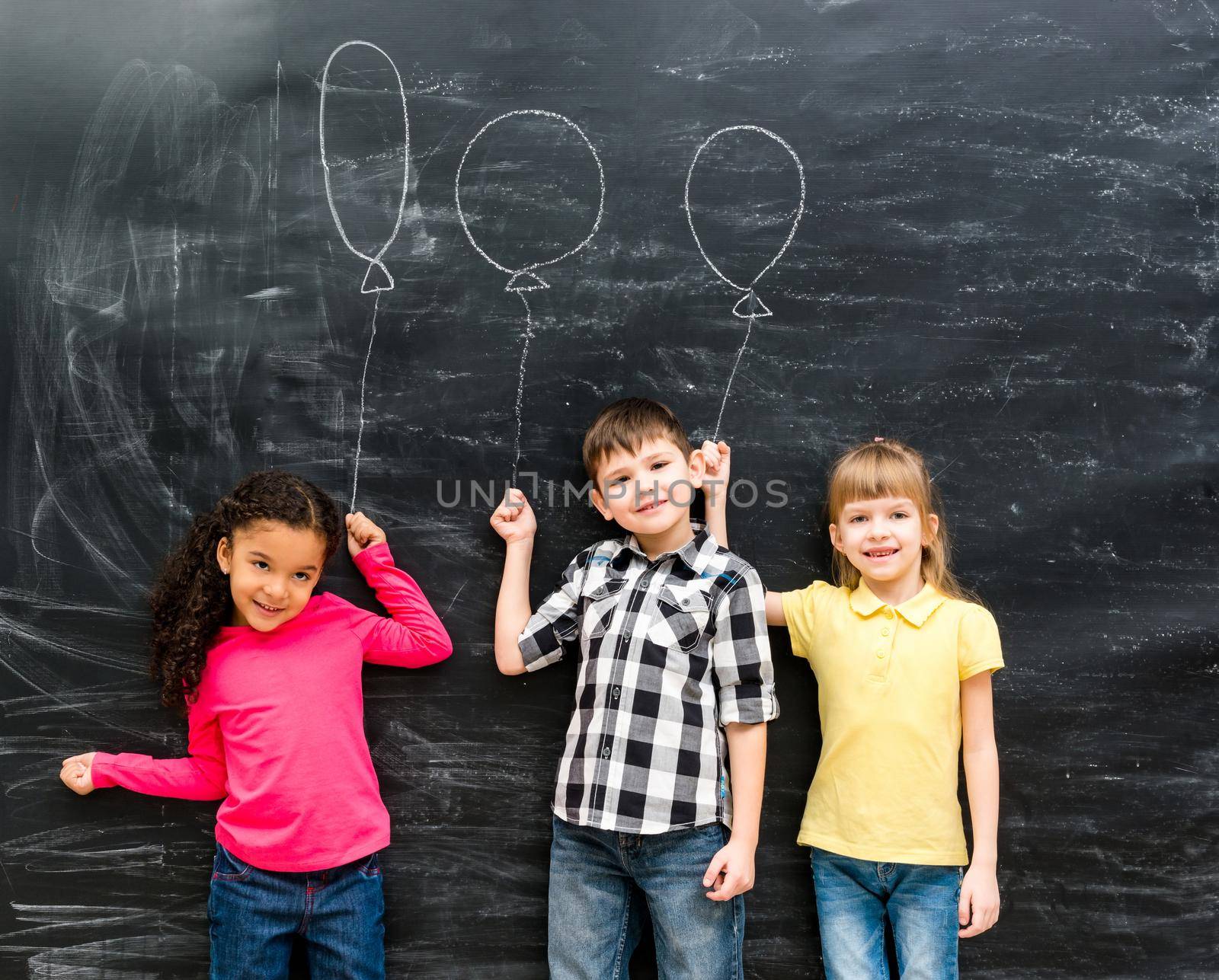 three joyful children keep imaginary balloons drawn on the blackboard by GekaSkr
