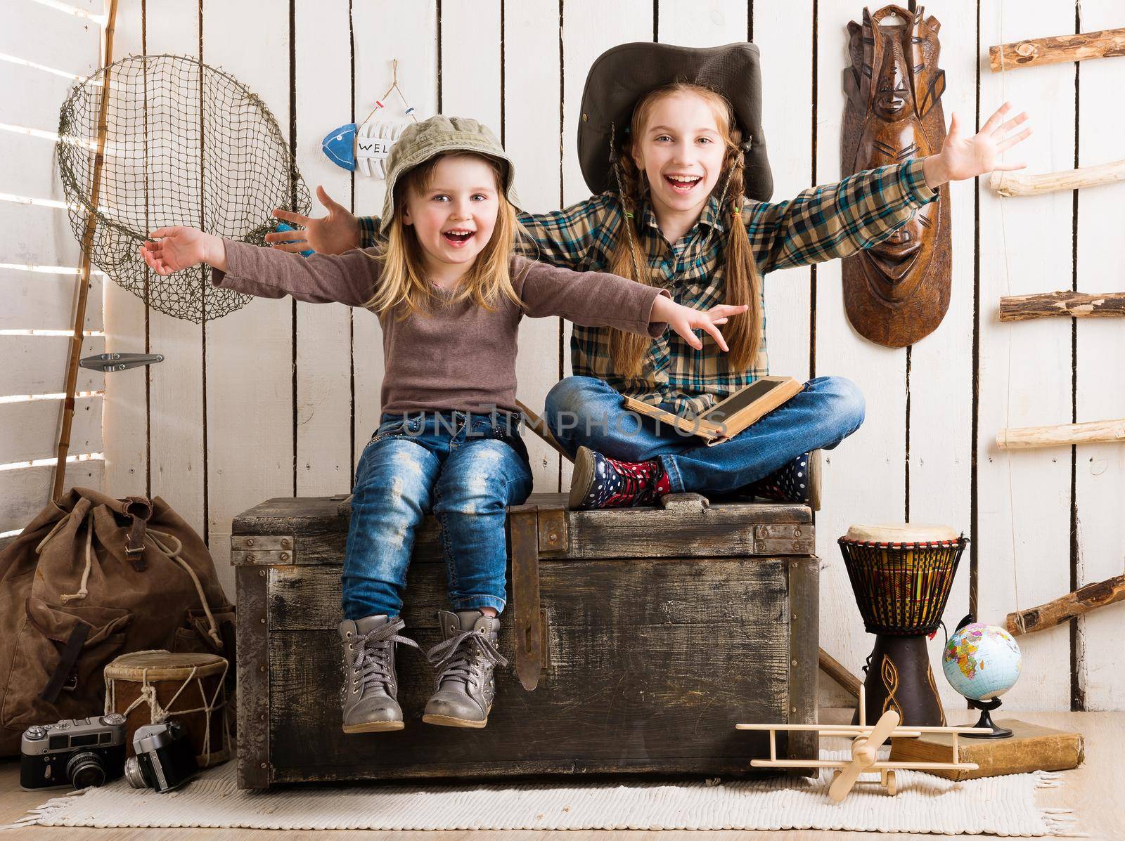 two little girls sitting on big wooden chest with hands up in cowboy hats