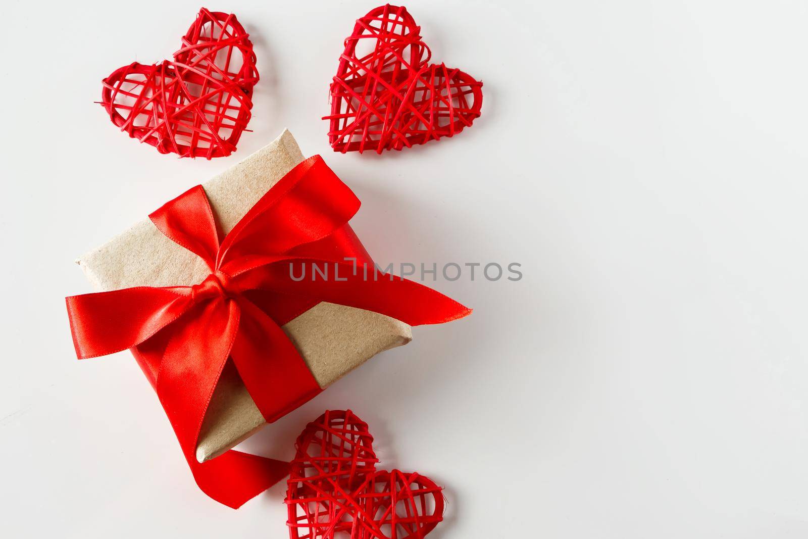 Valentine's day gift and red hearts on a white background. Holiday background for Valentine's day - a gift with a red satin ribbon and handmade hearts on a white background, photo for design.