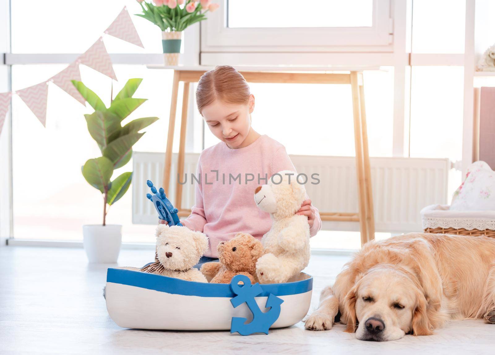 Little girl playing with marine toys on the floor and sitting close to sleeping golden retriever dog