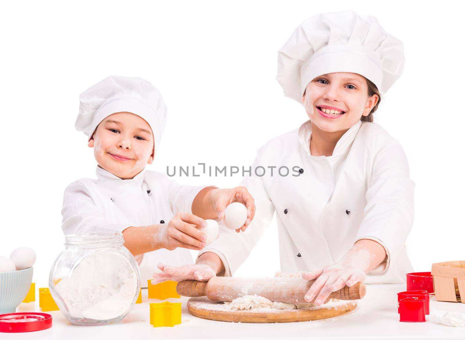two funny little cooks in white uniform preparing dough in the kitchen