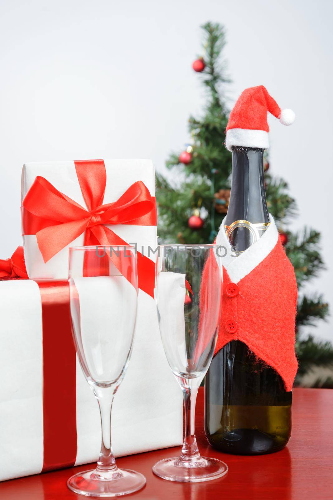 Present with red ribbon, a bottle of champagne on the background of Christmas tree