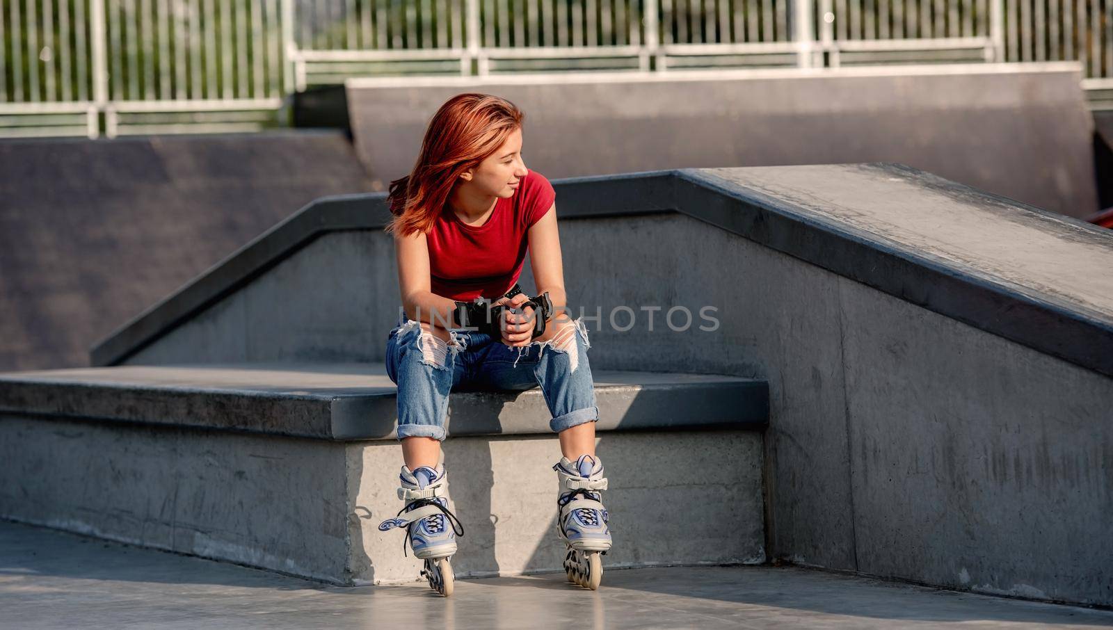 Pretty girl wearing roller skates sitting and looking back. Female teenager after rollerblading at summer portrait