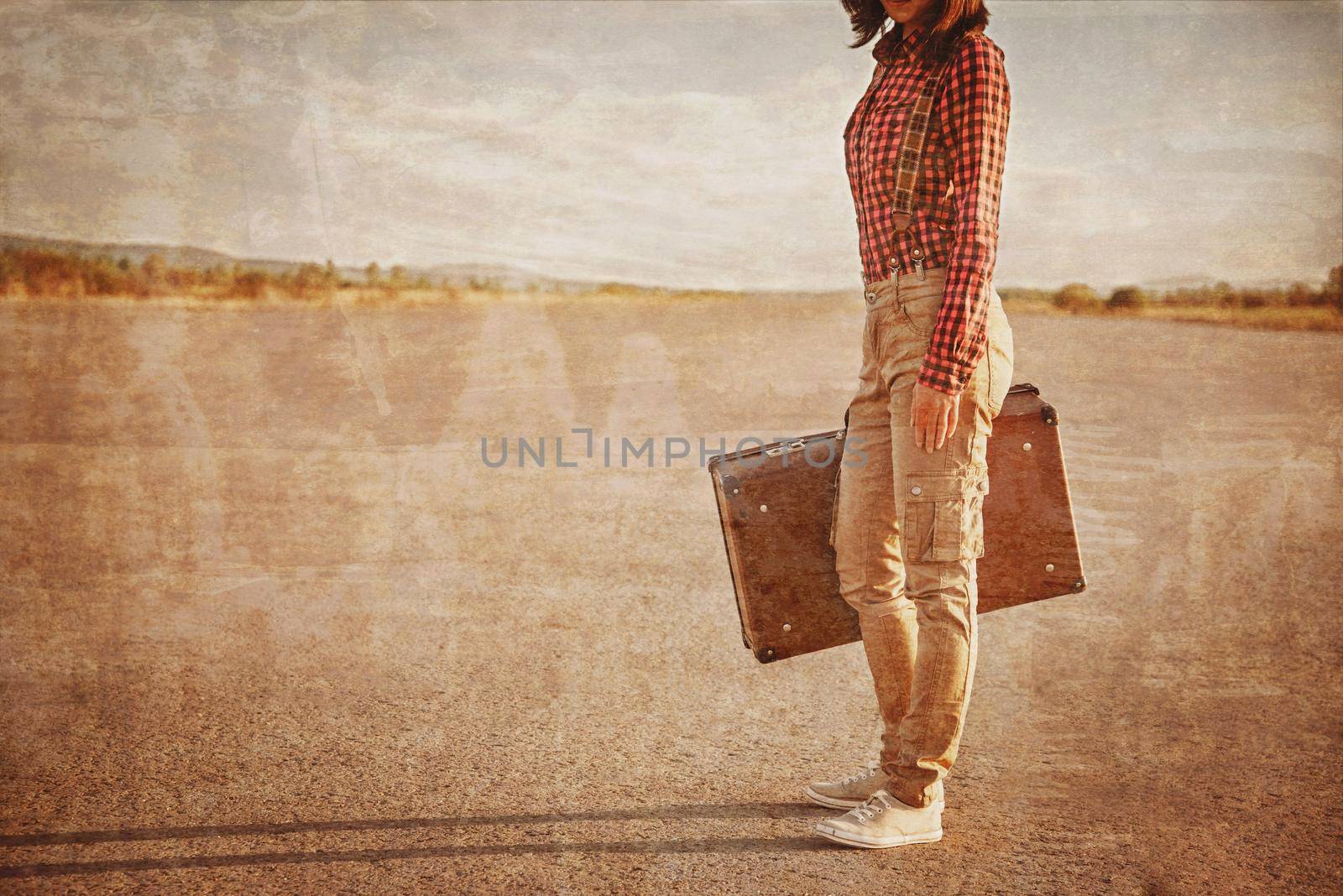 Unrecognizable woman is standing on road with vintage suitcase. Vintage image