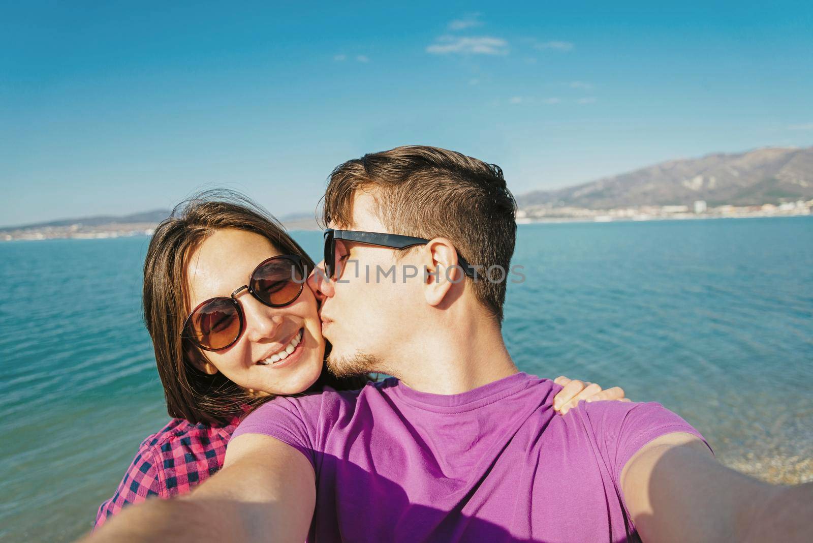 Happy young couple in love doing self-portrait on background of blue sea and man kissing a woman