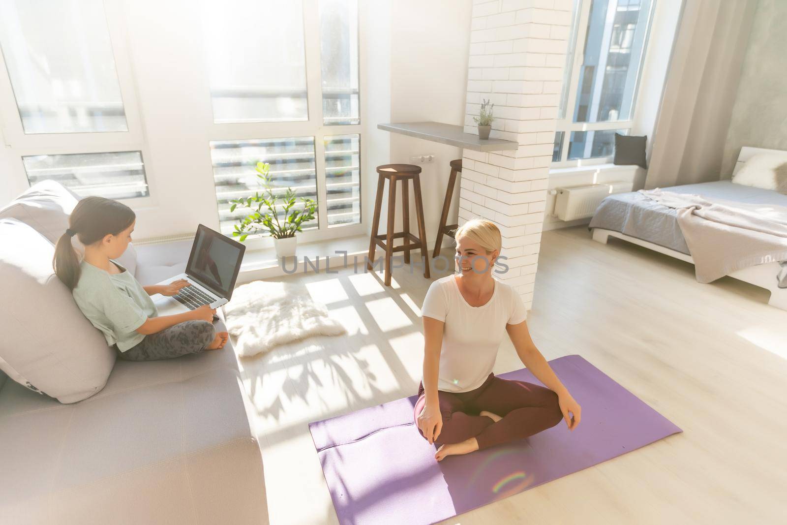 Time for yoga. Attractive young woman exercising and sitting in yoga lotus position while resting at home by Andelov13