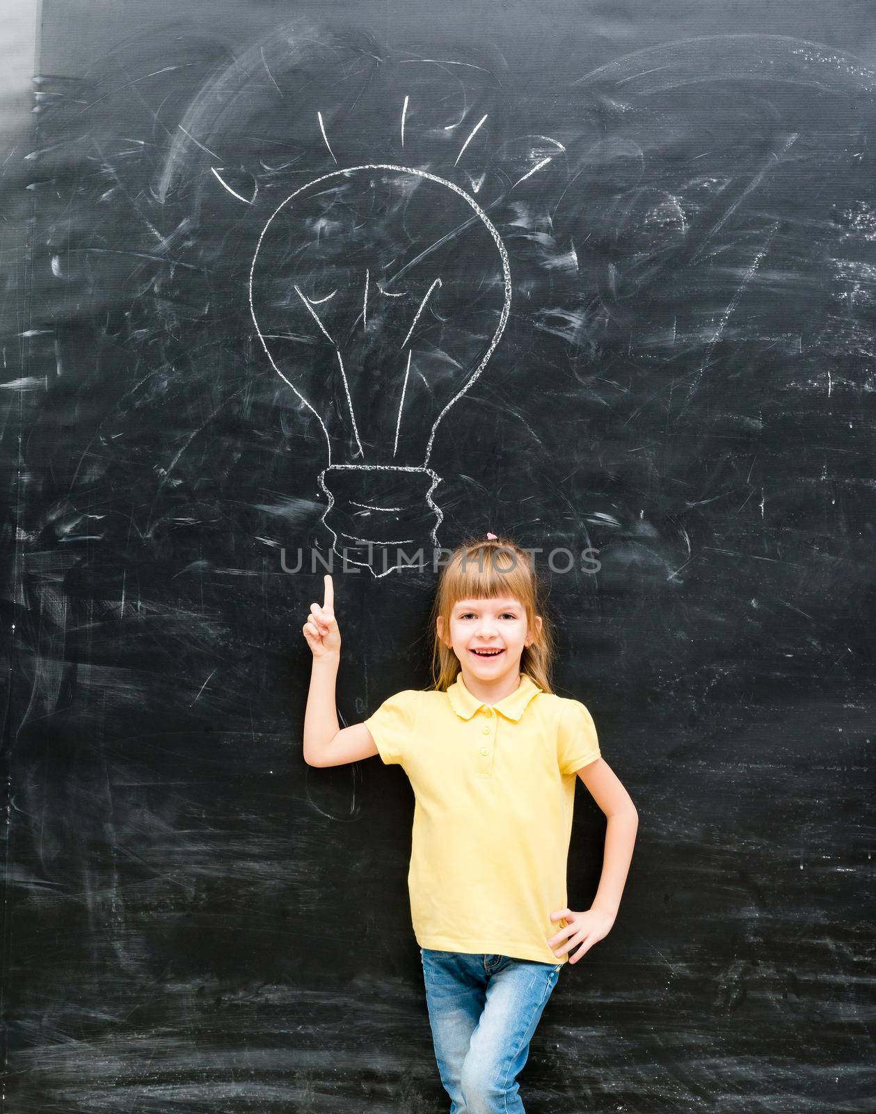 cute little boy with finger up having an idea with drawn lamp on chalky blackboard