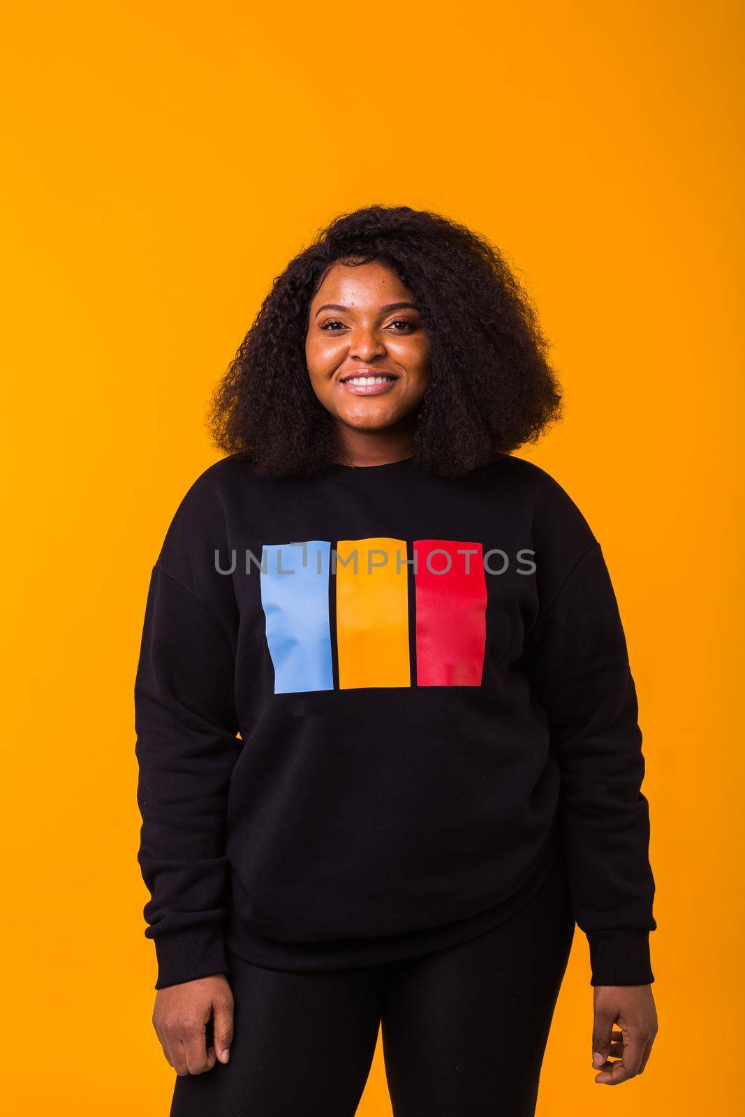 Youth street fashion concept - Confident sexy black woman in stylish hoodie having fun on yellow background. by Satura86