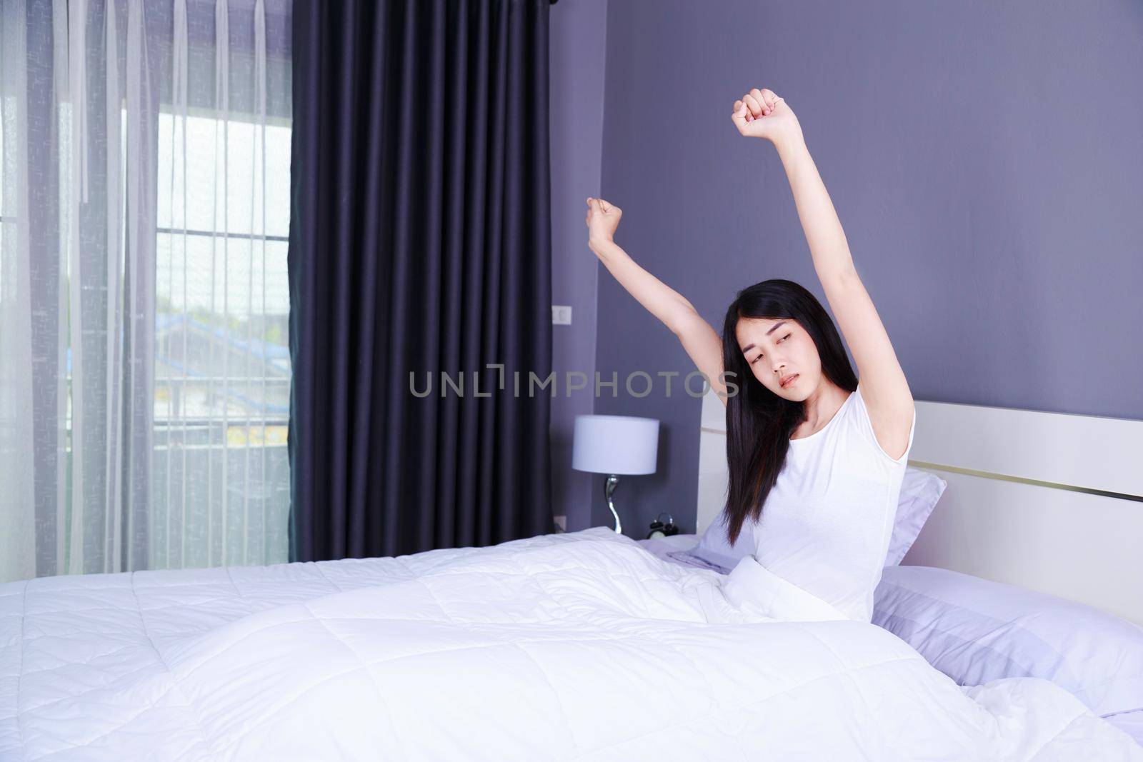 Woman waking up and hand raised on bed in the bedroom