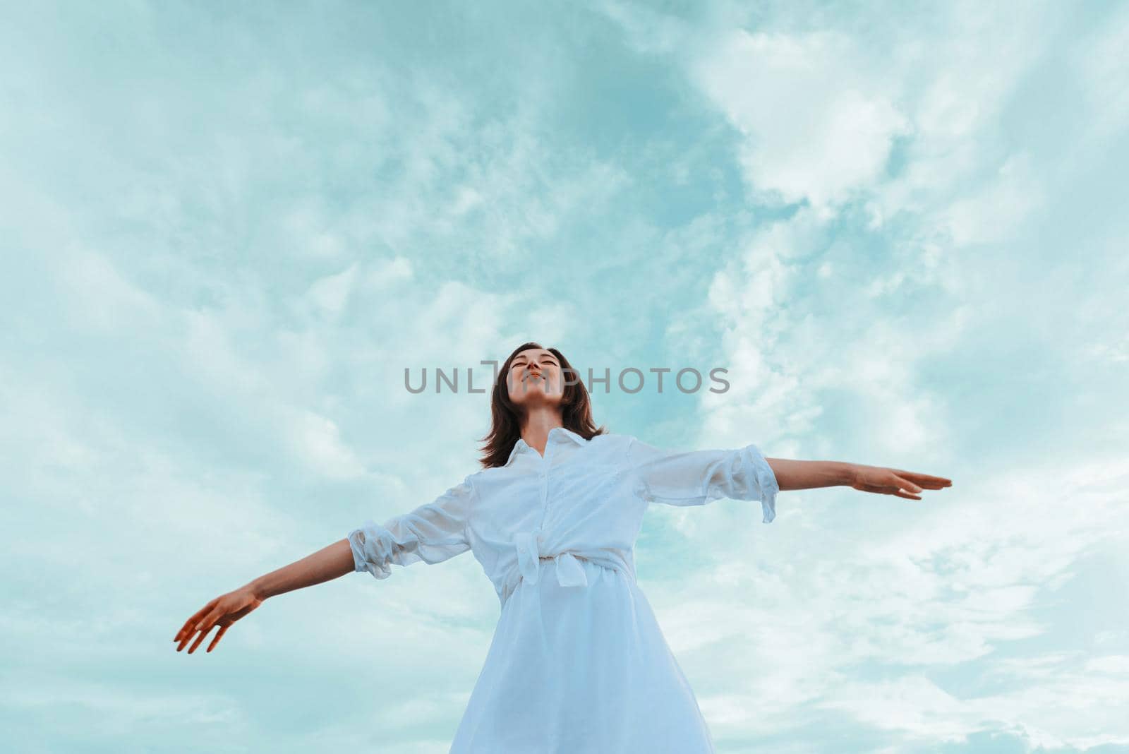 Beautiful young woman standing with raised arms and enjoying a nice day on a background of sky