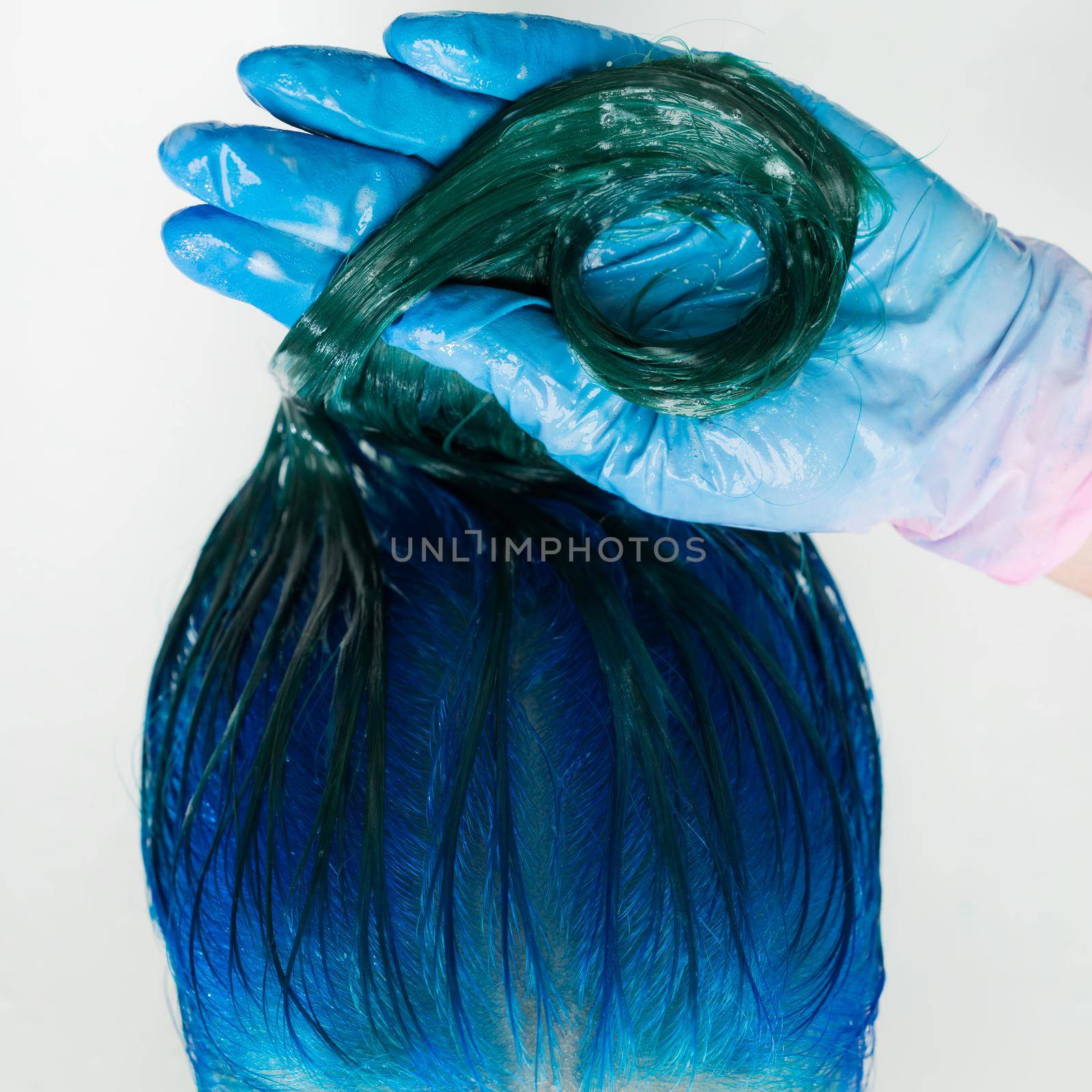 Washing of woman hair with conditioner shampoo in sink with special shower. High-angle shot of beautician in gloves washes customer long hair sapphire color after dyeing hair process in beauty salon.