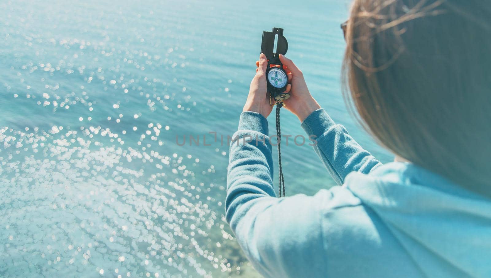 Traveler woman searching direction with a compass on coast near the sea in summer. Rear view