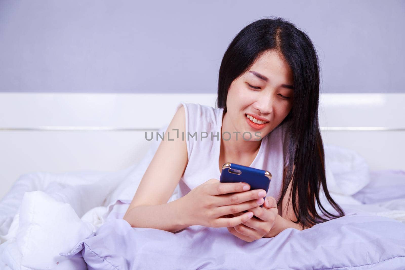 happy woman using a phone in her hand on bed in the bedroom