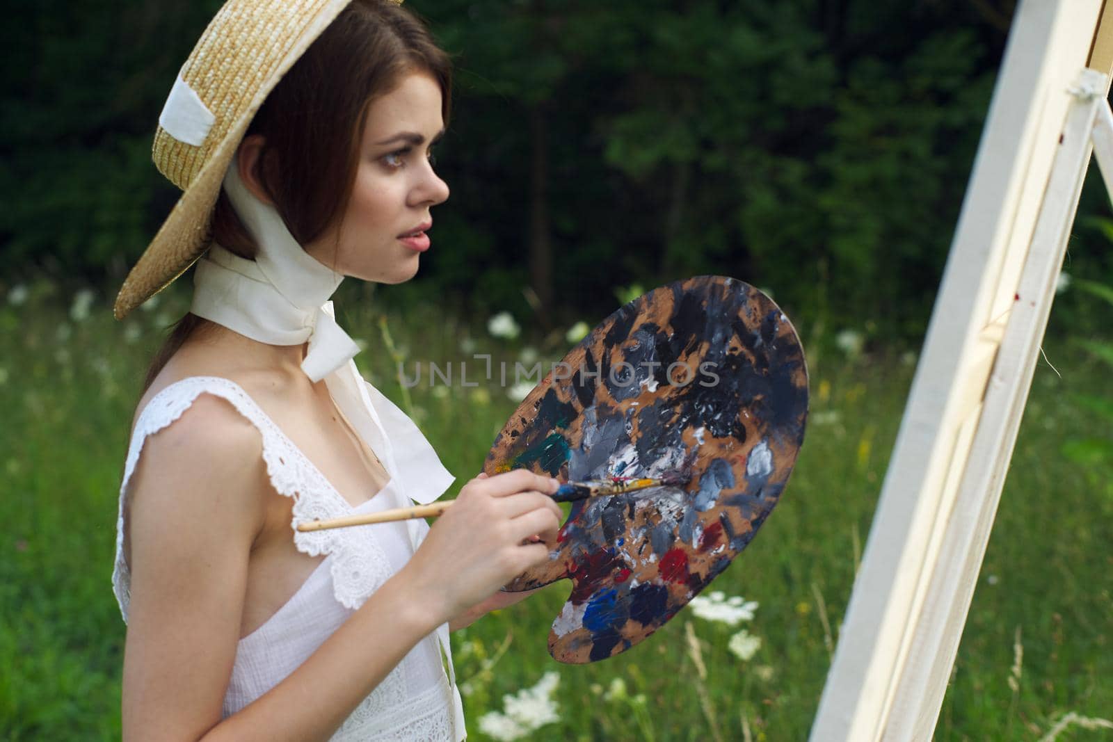 woman with a palette of paints painting a picture outdoors close-up. High quality photo